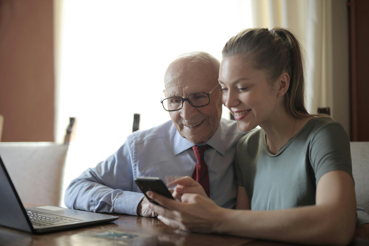 adult daughter showing her senior father an app on her phone